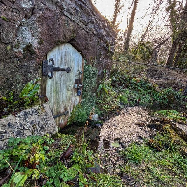  grey stone building with a small door by a stream. grey stone building with blue sky