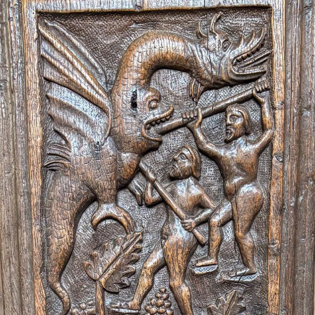  a wood carving depicting a dragon battling two men